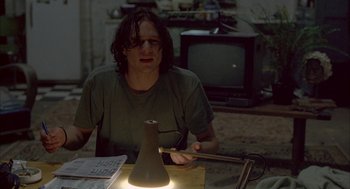 Movie still from “Candy” (2006), directed by Neil Armfield – A man sitting at a table with a lamp in front of him; Medium shot, Low angle