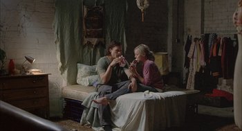 Movie still from “Candy” (2006), directed by Neil Armfield – Two women sitting on a bed and one of the women is eating a donut; Wide shot, High angle