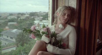 Movie still from “Candy” (2006), directed by Neil Armfield – A woman sitting on a window ledge holding a bouquet of flowers; Medium shot, Over the shoulder angle