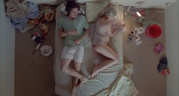 Movie still from “Candy” (2006), directed by Neil Armfield – A man and a woman laying on a bed reading; Wide shot, Overhead angle