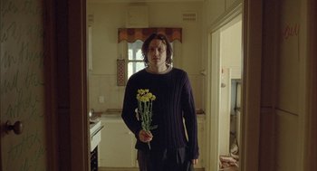 Movie still from “Candy” (2006), directed by Neil Armfield – A man holding a bunch of flowers in a kitchen; Medium shot, Low angle