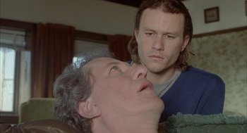 Movie still from “Candy” (2006), directed by Neil Armfield – A man standing next to another man on a couch; Close Up shot, Over the shoulder angle