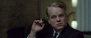 Movie still from “Capote” (2005), directed by Bennett Miller – A man in a suit and tie holding a cigarette in his hand; Close Up shot, Over the shoulder angle