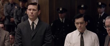 Movie still from “Capote” (2005), directed by Bennett Miller – Two men in suits stand in front of a police officer; Medium shot, Low angle