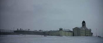 Movie still from “Capote” (2005), directed by Bennett Miller – A large building that has a fence around it; Extreme Wide shot, High angle