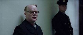 Movie still from “Capote” (2005), directed by Bennett Miller – A man in a black coat and glasses; Close Up shot, Over the shoulder angle