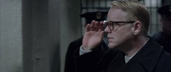 Movie still from “Capote” (2005), directed by Bennett Miller – A man in a suit and glasses saluting in a jail cell; Close Up shot, Over the shoulder angle