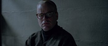 Movie still from “Capote” (2005), directed by Bennett Miller – A man wearing glasses and a sweater is staring straight ahead; Close Up shot, Over the shoulder angle