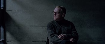 Movie still from “Capote” (2005), directed by Bennett Miller – A man sitting in front of a brick wall with his arms crossed; Medium shot, Over the shoulder angle