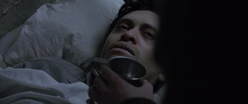 Movie still from “Capote” (2005), directed by Bennett Miller – A man laying in a bed holding a metal cup; Close Up shot, High angle