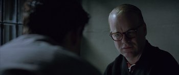 Movie still from “Capote” (2005), directed by Bennett Miller – A man with glasses is looking at another man in a dark room; Close Up shot, Over the shoulder angle