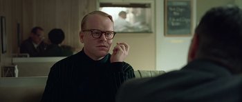 Movie still from “Capote” (2005), directed by Bennett Miller – A man sitting on a couch in a living room; Close Up shot, Over the shoulder angle