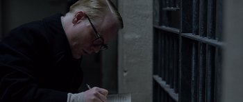 Movie still from “Capote” (2005), directed by Bennett Miller – A man writing on a piece of paper in front of a jail cell; Close Up shot, High angle