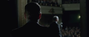 Movie still from “Capote” (2005), directed by Bennett Miller – A man in a black suit is standing in front of an audience; Close Up shot, Over the shoulder angle