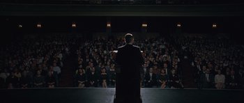 Movie still from “Capote” (2005), directed by Bennett Miller – A man in a black suit is giving a speech to an audience; Extreme Wide shot, High angle
