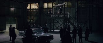 Movie still from “Capote” (2005), directed by Bennett Miller – A group of people standing in a warehouse; Extreme Wide shot, High angle