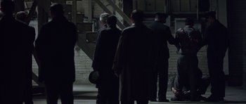 Movie still from “Capote” (2005), directed by Bennett Miller – A group of people standing in a dark room next to a staircase; Wide shot, High angle