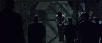 Movie still from “Capote” (2005), directed by Bennett Miller – A group of people standing around in a dark room; Wide shot, Over the shoulder angle