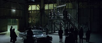 Movie still from “Capote” (2005), directed by Bennett Miller – A group of people standing around a car in a building; Extreme Wide shot, High angle