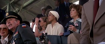 Movie still from “Capricorn One” (1977), directed by Peter Hyams – A group of people standing in a stadium watching a baseball game; Medium shot, Over the shoulder angle