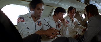 Movie still from “Capricorn One” (1977), directed by Peter Hyams – A group of men sitting next to each other on top of a plane; Medium shot, Low angle