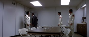 Movie still from “Capricorn One” (1977), directed by Peter Hyams – A group of men standing around a table in a room; Wide shot, Over the shoulder angle
