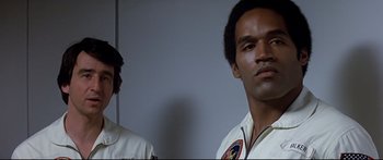 Movie still from “Capricorn One” (1977), directed by Peter Hyams – Two men standing next to each other in front of a white wall; Close Up shot, Low angle