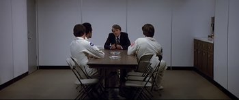 Movie still from “Capricorn One” (1977), directed by Peter Hyams – A group of people sitting around a table; Wide shot, Over the shoulder angle