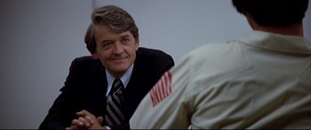 Movie still from “Capricorn One” (1977), directed by Peter Hyams – A man in a suit and tie sitting next to another man in a suit; Close Up shot, Over the shoulder angle