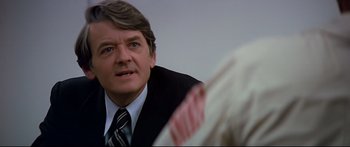 Movie still from “Capricorn One” (1977), directed by Peter Hyams – A person wearing a suit and tie; Close Up shot, Over the shoulder angle