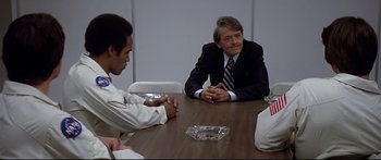 Movie still from “Capricorn One” (1977), directed by Peter Hyams – A group of people sitting around a table; Medium shot, Over the shoulder angle