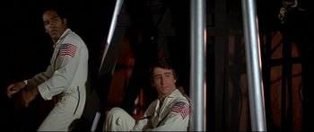 Movie still from “Capricorn One” (1977), directed by Peter Hyams – A man sitting in a chair with a flag on his shoulder; Medium shot, Low angle