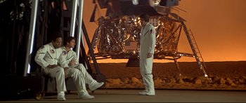 Movie still from “Capricorn One” (1977), directed by Peter Hyams – Two men in white suits standing next to each other on a dirt field; Wide shot, High angle