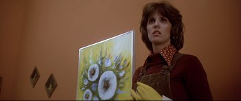 Movie still from “Capricorn One” (1977), directed by Peter Hyams – A woman holding up a painting while wearing gloves; Medium shot, Low angle
