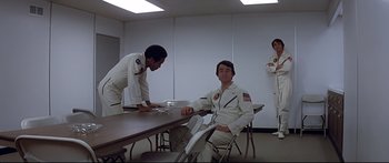 Movie still from “Capricorn One” (1977), directed by Peter Hyams – A group of men in white suits sitting at a table; Wide shot, Low angle