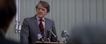 Movie still from “Capricorn One” (1977), directed by Peter Hyams – A man standing at a podium with microphones in front of him; Close Up shot, Low angle