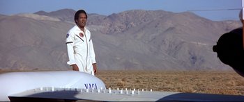 Movie still from “Capricorn One” (1977), directed by Peter Hyams – A man standing in front of an object in the desert; Wide shot, Low angle