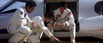 Movie still from “Capricorn One” (1977), directed by Peter Hyams – A group of men sitting on the ground; Medium shot, Low angle