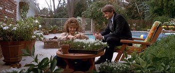 Movie still from “Capricorn One” (1977), directed by Peter Hyams – A man and a woman sitting at a table with plants; Medium shot, Low angle
