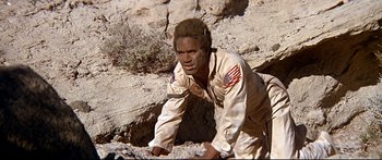 Movie still from “Capricorn One” (1977), directed by Peter Hyams – An african american man climbing up a rocky hill; Medium shot, Low angle