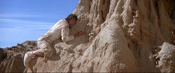 Movie still from “Capricorn One” (1977), directed by Peter Hyams – A man climbing up a rock wall in the desert; Wide shot, Low angle