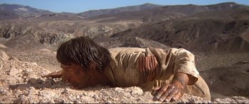Movie still from “Capricorn One” (1977), directed by Peter Hyams – A man is laying on the ground in the desert; Wide shot, Low angle