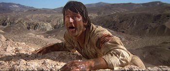 Movie still from “Capricorn One” (1977), directed by Peter Hyams – A man in a dirt field covered in mud; Medium shot, Low angle