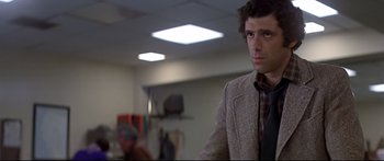 Movie still from “Capricorn One” (1977), directed by Peter Hyams – A man standing in a room looking at the camera; Close Up shot, Over the shoulder angle