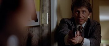 Movie still from “Capricorn One” (1977), directed by Peter Hyams – A man holding a gun while sitting in a room; Close Up shot, Over the shoulder angle