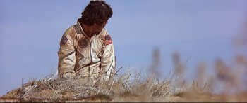 Movie still from “Capricorn One” (1977), directed by Peter Hyams – A man in a field with an american flag on his shirt; Wide shot, Low angle