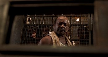 Movie still from “Carandiru” (2003), directed by Hector Babenco – A man in a prison cell with a gun in his hand; Medium shot, Low angle
