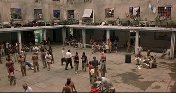 Movie still from “Carandiru” (2003), directed by Hector Babenco – A group of people standing around in a courtyard; Extreme Wide shot, High angle
