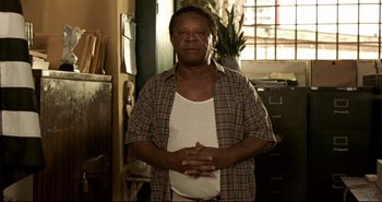 Movie still from “Carandiru” (2003), directed by Hector Babenco – An older man standing in front of a window; Medium shot, Low angle