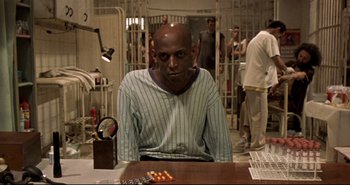 Movie still from “Carandiru” (2003), directed by Hector Babenco – A man sitting at a table in a jail cell; Medium shot, Low angle